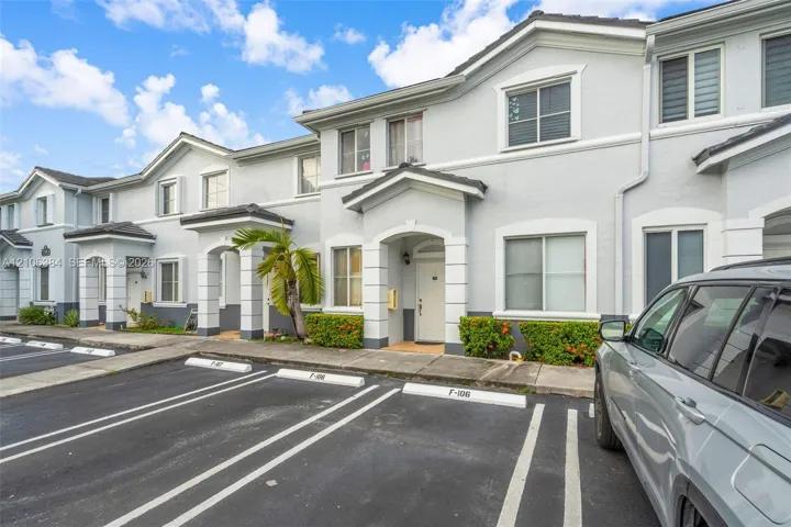Multi-level exterior facade featuring a neutral stucco finish, decorative stone-textured corner quoins, gable rooflines, covered entryways, and assigned asphalt parking spaces