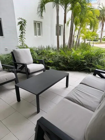 Covered patio featuring light-toned tile flooring, stucco exterior wall, and lush palm tree landscaping