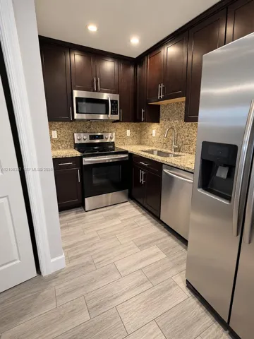 Kitchen featuring dark wood-finish cabinetry, speckled stone countertops, stainless steel appliances, and wood-finish flooring