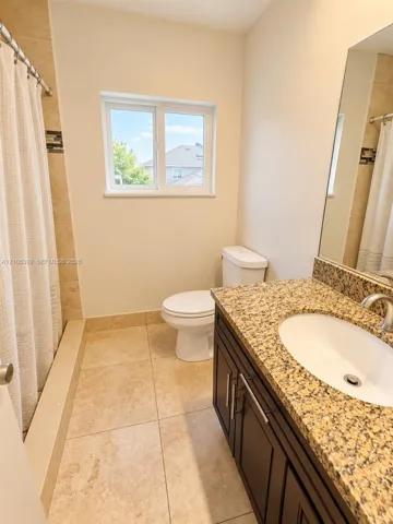 Bathroom featuring a dark wood-finish vanity with a stone countertop, undermount sink, tile flooring, and a tiled shower surround with a decorative mosaic accent