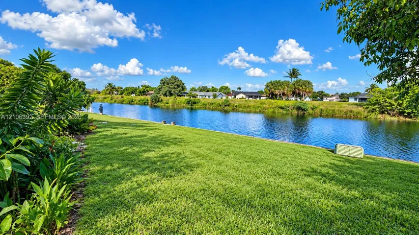 Waterfront backyard featuring a manicured lawn, concrete seawall, and mature greenery