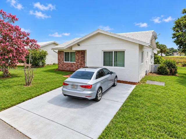 Single-story exterior featuring white stucco siding, brick veneer accents, a gabled roofline with tile shingles, and a concrete driveway
