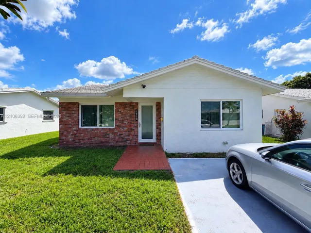 Single-story residence featuring a painted stucco exterior, brick facade detailing, a concrete driveway, and a tile roof