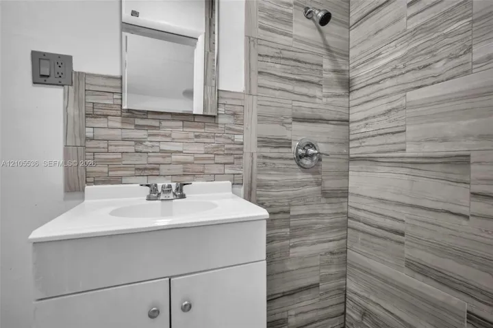Bathroom vanity featuring a white cabinet, integrated sink, chrome faucet, and mosaic tile backsplash, accompanied by a shower enclosure finished in large-format linear-patterned tile with chrome fixtures