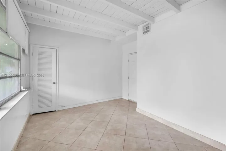 Interior space featuring exposed beam ceilings, large windows, tile flooring, and louvered closet doors