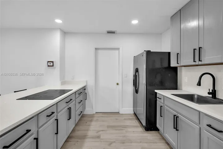 Shaker-style cabinetry with matte black hardware, quartz countertops, integrated cooktop, undermount stainless steel sink with high-arc faucet, and wood-finish flooring
