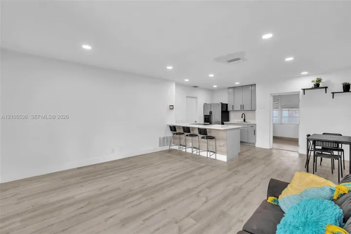 Open-concept kitchen featuring light grey cabinetry, stone-finish countertops, an integrated breakfast bar, recessed lighting, and wood-finish flooring throughout