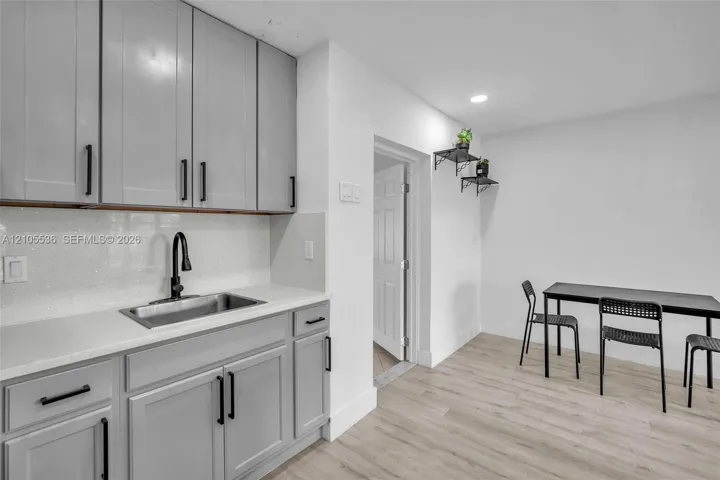 Kitchenette featuring gray shaker-style cabinetry, matte black hardware, light-toned stone-surface countertops, a stainless steel sink with a matte black high-arc faucet, and wood-finish flooring