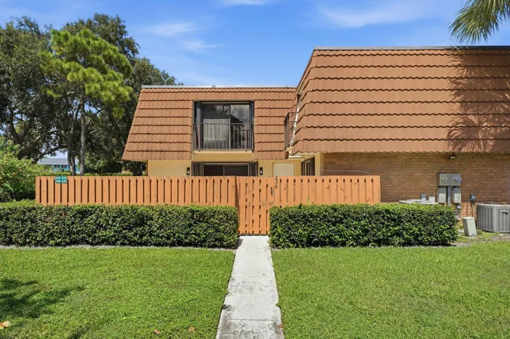 Pitched roofline with textured tiles, upper-level balcony with metal railing, privacy fencing, and a manicured lawn