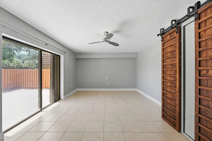 Barn Doors open to a murphy bed. Spacious open room with neutral gray walls, ceiling fan, and tile flooring throughout.