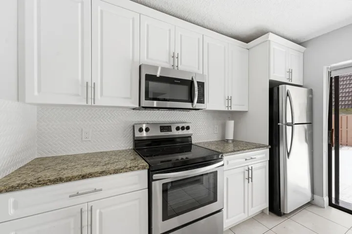 White cabinetry with stainless steel appliances, stone countertops, and a herringbone tile backsplash