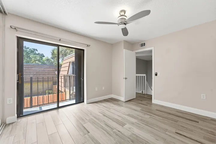 Sliding glass door to balcony, wood-finish flooring, ceiling fan, and white trim