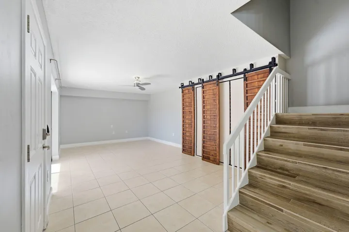Wood-finish staircase with white railings, tile flooring, and wood-paneled barn doors with black hardware