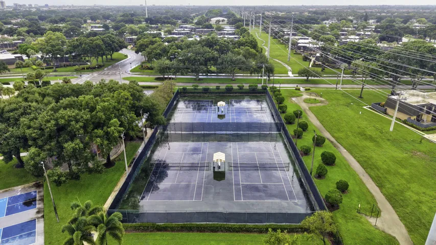 Two hard-surface tennis courts with perimeter fencing, surrounded by manicured lawns and mature trees