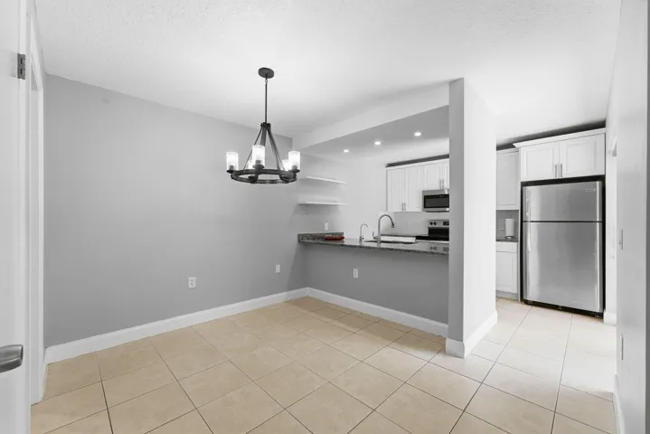Open concept layout with tile flooring, a contemporary chandelier, kitchen with white cabinetry, stainless steel appliances, and a breakfast bar with stone countertops