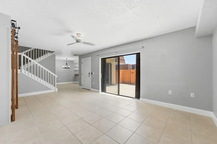 Tiled flooring, white staircase with railing, sliding glass door, ceiling fan, and built-in shelving