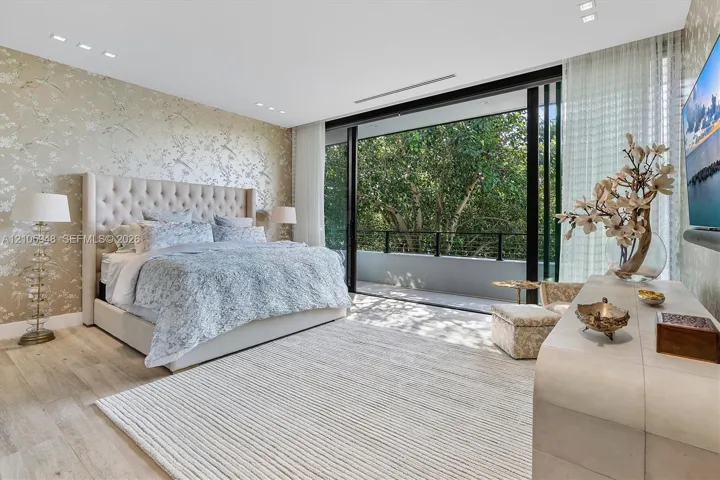 Floor-to-ceiling sliding glass doors opening to a balcony, light-toned wood-finish flooring, recessed ceiling lighting, and patterned wallpaper feature wall