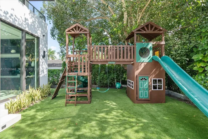 Outdoor area featuring low-maintenance synthetic turf, integrated wood play structure with dual towers and slide, and established perimeter privacy hedging