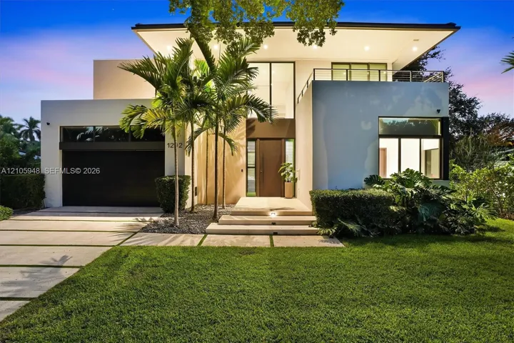 Contemporary architectural exterior featuring a stucco facade, second-story balcony with metal railing, oversized glass entryway, and a concrete paver driveway