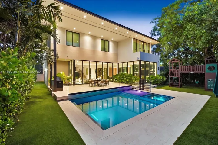 Contemporary multi-level exterior with floor-to-ceiling glass wall systems, paved stone patio, integrated swimming pool with built-in spa, and artificial turf lawn