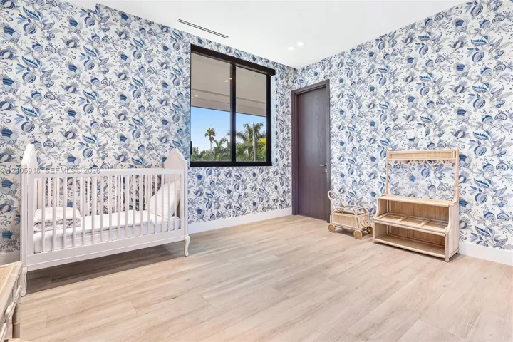 Room featuring floral patterned wallpaper, light wood-finish flooring, a black-framed window, and a dark wood-finish interior door with recessed ceiling lighting