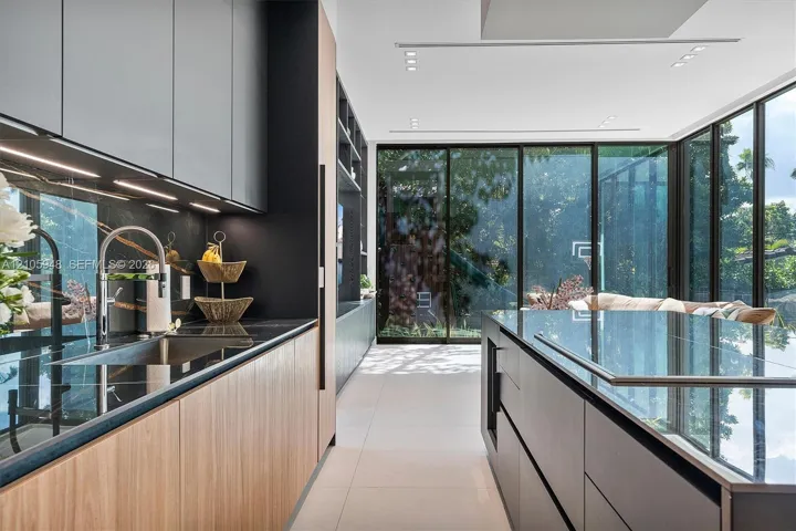 Modern kitchen featuring matte cabinetry, wood-finish lower cabinetry, integrated dark stone-surface countertops, floor-to-ceiling glass panel walls, and recessed ceiling lighting