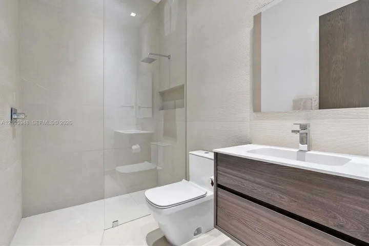 Floating vanity with wood-finish cabinetry, white countertop, integrated sink, rainfall shower head, and full-height glass shower panel