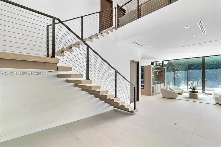 Floating staircase with wood-finish treads and horizontal cable railing, large-format tile flooring, and expansive floor-to-ceiling glass wall panels
