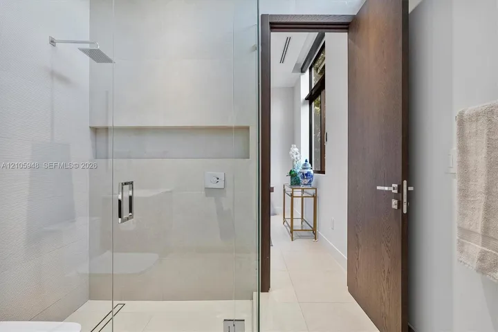 Walk-in shower featuring glass enclosure, wall-mounted rainfall showerhead, and integrated recessed shelving, complemented by a solid wood-finish door with brushed metal hardware