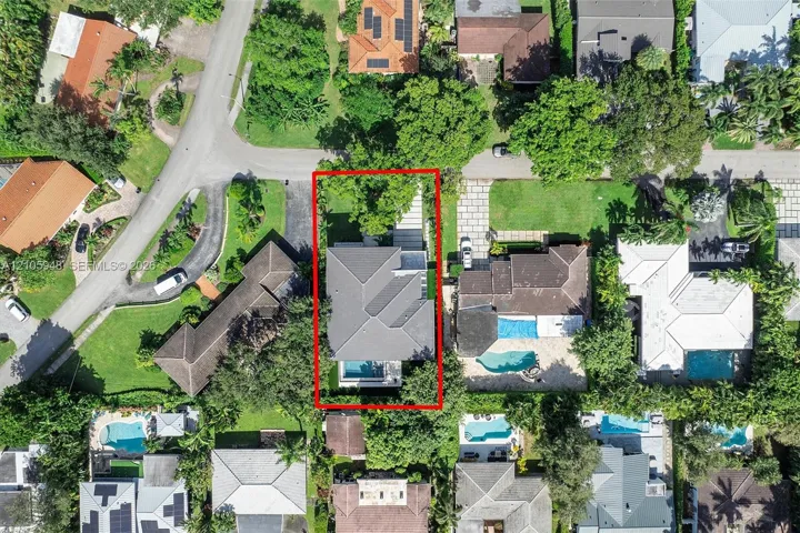 Aerial view of a residential property featuring a hipped roof, paved driveway, swimming pool, and established perimeter landscaping