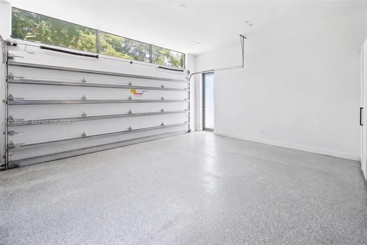 Garage space featuring speckled epoxy flooring, white paneled walls, a ceiling-mounted automatic door opener, and a row of horizontal transom windows