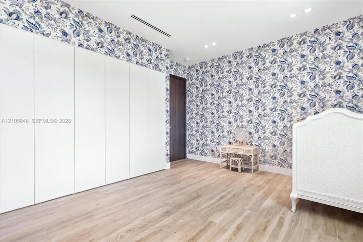 Room featuring floor-to-ceiling white cabinetry, wood-finish flooring, patterned wallpaper, recessed lighting, and a dark-finish door