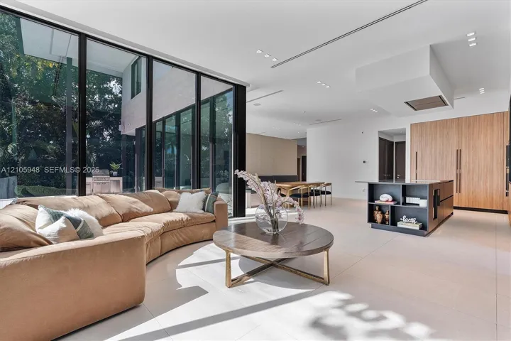 Floor-to-ceiling glass walls, integrated light-toned cabinetry, a modern kitchen island with built-in shelving, recessed ceiling lighting, and large-format tile flooring
