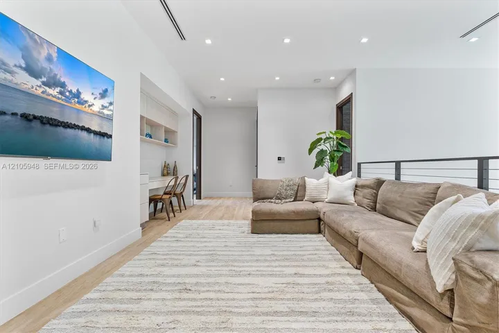 Open-concept space featuring wood-finish flooring, recessed lighting, built-in desk cabinetry, and a metal-rail staircase