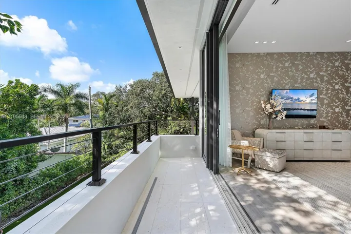 Covered balcony with stone-tile flooring and black metal railing featuring horizontal cable infill, highlighted by large-format retractable glass doors