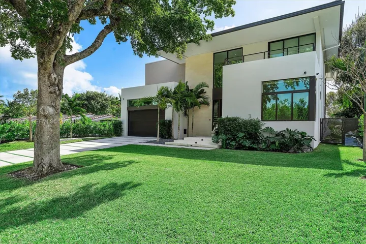 Modern two-story architectural exterior featuring smooth stucco siding, large-pane windows, a second-level balcony with metal railing, and a paved multi-car driveway