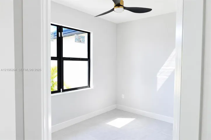 Neutral-toned room featuring a matte black three-blade ceiling fan with gold accents, large-format tile flooring, and a single-hung window with a matte black frame