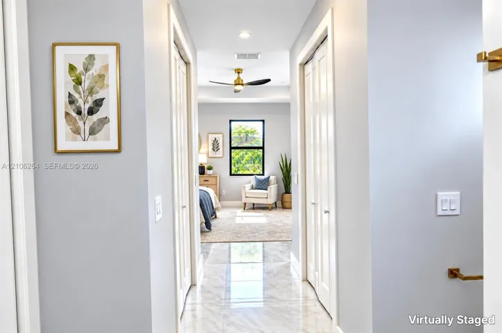Hallway featuring polished stone-finish tile flooring, dual closet storage with bi-fold doors, and a brass-finish ceiling fan with integrated lighting