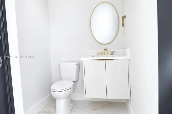 Floating vanity with integrated countertop and backsplash, brass-toned hardware, oval-framed mirror, and large-format tile flooring