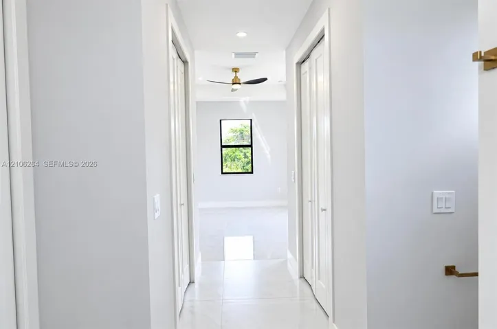 Hallway featuring light-toned tile flooring, recessed lighting, dual bi-fold closet doors, and metallic hardware fixtures
