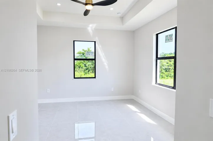 Room featuring neutral tile flooring, a tray ceiling, recessed lighting, a modern ceiling fan, and black-framed windows