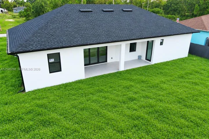 Rear elevation featuring a hip roof with integrated skylights, a covered patio with concrete flooring, and black-framed windows and doors