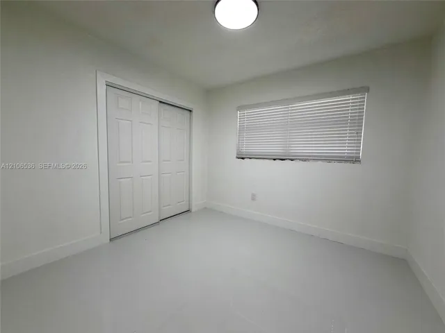 Interior room featuring polished tile flooring, white walls, a dual-panel sliding closet, and a horizontal blind-covered window