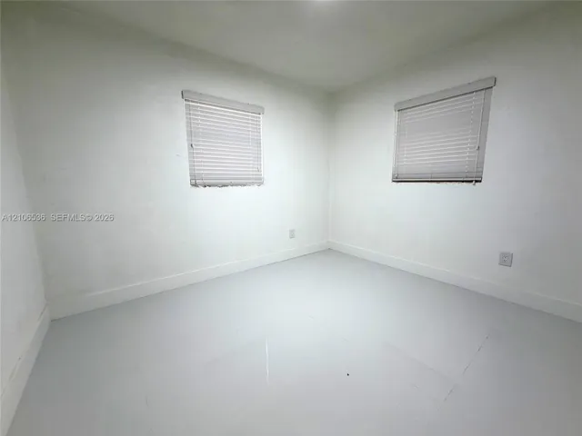 Interior room featuring uniform wall finish, dual windows with integrated horizontal blinds, and smooth-finish flooring