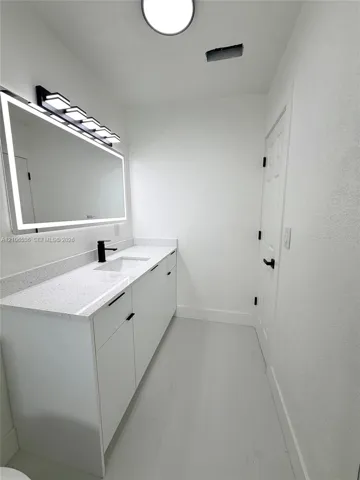 Modern vanity with a speckled countertop, integrated rectangular sink, matte black faucet, and a large backlit mirror with an integrated light fixture