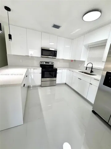 Kitchen featuring high-gloss white cabinetry, quartz countertops, large-format tile flooring, stainless steel appliances, and a matte black gooseneck faucet