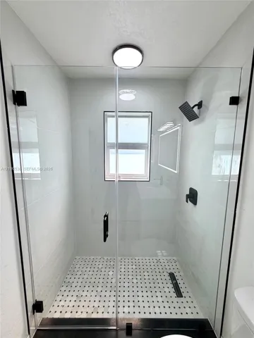 Walk-in shower featuring a frameless glass enclosure, matte black fixtures, white tiled walls, patterned floor tiling, and a recessed ceiling light