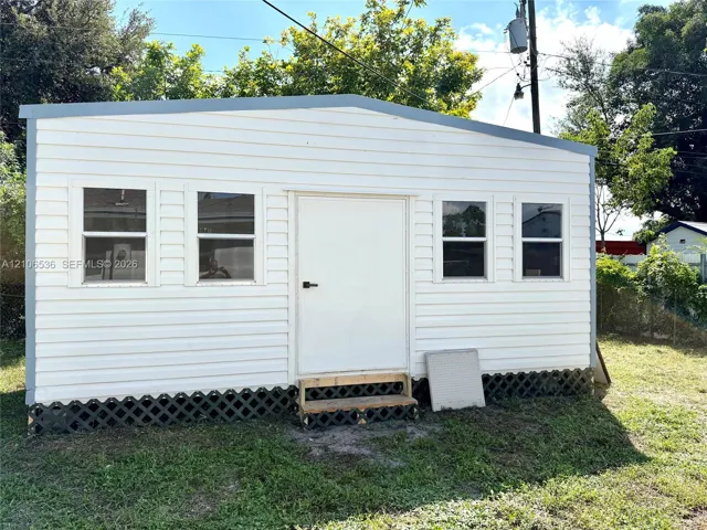 Exterior structure featuring horizontal siding, a sloped roofline, four rectangular windows, and lattice skirting