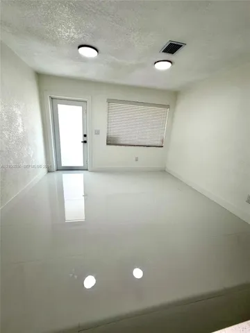 Polished large-format tile flooring, textured wall finish, dual flush-mount ceiling lighting, and a glass-paneled entry door