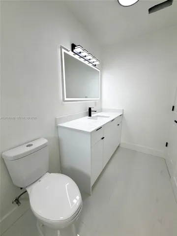 White vanity featuring a light-toned solid surface countertop, rectangular undermount sink, matte black faucet, and an integrated LED-backlit mirror